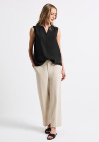 Černý bezramínkový top s výstřihem do V, kombinovaný s volnými béžovými kalhotami. Hladká textilie, jednoduchý design a ploché černé sandály.