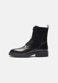 Bota negra de cuero hasta el tobillo con punta redonda, frente con cordones, tira de agarre y suela texturizada. Acabado suave y diseño minimalista.