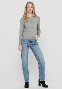 Grauer Strickpullover mit einem runden Ausschnitt, kombiniert mit hellblauen, geraden Jeans. Das Modell trägt schwarze, enganliegende Stiefeletten mit Absatz. Ein schlichter, lässiger Look.