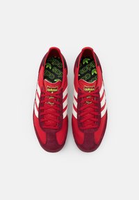 Röda sneakers med en mix av slät tyg och mocka. Tre vita ränder på sidorna, accentuerade med en grön logotyp på en texturerad innersula.