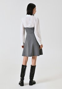 Grau gestreiftes Kleid mit tailliertem Oberteil und schwingendem Rock, ausgestattet mit einer weißen Blusen-ähnlichen Oberseite mit Puffärmeln und schwarzen knielangen Stiefeln.