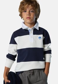 Polo a maniche lunghe a righe navy e bianche con colletto, dotato di patch con logo e polsini in maglia, abbinato a pantaloni pantaloni corti grigi chiari.