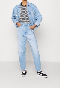 Chaqueta de mezclilla azul claro, camiseta de rayas en blanco y negro, jeans de tiro alto azul claro, zapatillas en blanco y negro, corte relajado, estilo casual.