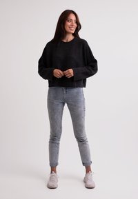 Czarny, prążkowany, krótki sweter z długimi rękawami, w połączeniu z jasnoniebieskimi obcisłymi dżinsami i jasnymi sneakersami. Gładkie tło.