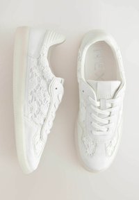 Sneakers bianchi con dettagli in pizzo sui lati, pelle testurizzata e punte lisce. Punta arrotondata e suola ammortizzata. I lacci passano attraverso cinque asole.