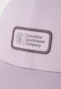 Ανοιχτό μωβ καπέλο μπέιζμπολ με ορθογώνιο ετικέτα της Columbia Sportswear Company, που απεικονίζει ένα λογότυπο με βουνό και δέντρο.