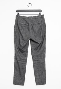 Pantaloni a griglia grigia con vestibilità sartoriale, dotati di doppie tasche posteriori e una texture liscia, appesi a una gruccia nera.
