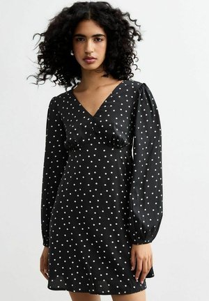 Zwarte jurk met witte stippen. V-hals, lange pofmouwen en een getailleerde taille. Gladde stof met een vloeiende silouet.