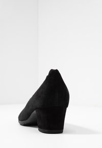 Escarpin en daim noir à talon haut, avec un bout pointu et un talon bloc moyen. Texture lisse avec une finition mate, sans quincaillerie ni motifs visibles.