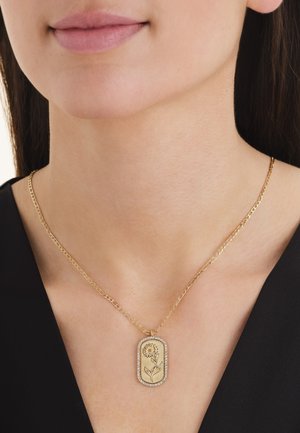 Collana con catena dorata e ciondolo rettangolare con un girasole inciso e un bordo di piccole pietre trasparenti sul collo di una donna.