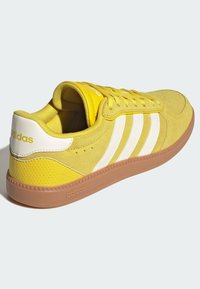 Gula mockasneakers med vita ränder, rundad tå, vadderad krage och gummisula. Märkeslogotyp på hälen och tungan.