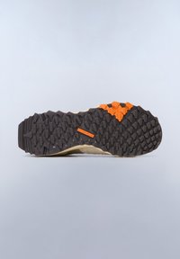 Podešev běžecké obuvi na trail s texturovaným černým gumovým vzorem, oranžovým akcentem a béžovou mezipodešví, navržena pro trakci a odolnost.