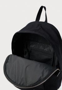 Mochila negra con el compartimento principal abierto, mostrando el interior acolchado y un bolsillo de malla con cremallera en el interior, contra un fondo neutro.