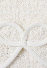 Tessuto bianco testurizzato con pizzo bianco intrecciato che forma una forma a fiocco, caratterizzato da una finitura morbida e pelosa e un leggero lucido.