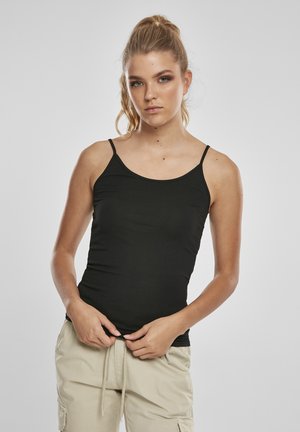 Schwarzes Tanktop mit dünnen Trägern, figurbetonter Schnitt, glatte Textur. Kombiniert mit hellen Cargo-Hosen steht das Model vor einem neutralen Hintergrund.