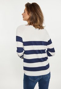 Gestreifter Pullover in Weiß und Marineblau mit rundem Halsausschnitt, langen Ärmeln und lockerer Passform, kombiniert mit blauen Jeans.