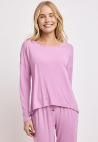 Jasnoróżowa bluzka z długim rękawem, okrągłym dekoltem i luźnym krojem. Wykonana z miękkiego, gładkiego materiału w casualowym stylu. W komplecie ze spodniami w tym samym kolorze.