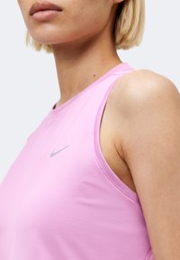 Κοντινό πλάνο ενός ατόμου που φοράει ένα ροζ αμάνικο τοπ Nike, εμφανίζοντας το λαιμό, τον ώμο και το πάνω μέρος του στήθους.