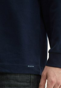 Navyblaues Langarmhemd aus Baumwolle mit abgerundetem Saum und sichtbarem TOM TAILOR Markenlabel an der unteren Seite.