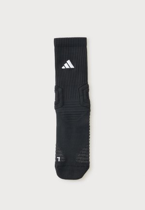 Μαύρη αθλητική κάλτσα Adidas με ραβδωτή υφή, επενδυόμενες περιοχές, λευκό λογότυπο κοντά στην κορυφή και ένδειξη αριστερού ποδιού στη μύτη.