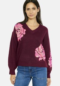 Maglione bordeaux con scollatura a V e maniche lunghe, caratterizzato da disegni di rose in paillettes rosa su entrambi i lati. Tessuto lavorato morbido.
