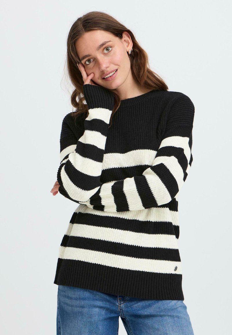 Schwarz- und cremefarbener gestreifter Pullover mit gerippter Textur, lange Ärmel und runder Ausschnitt. Getragen über einer blauen Jeans.