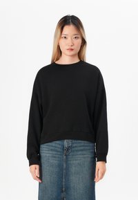 Sweatshirt noir court avec des manches longues, un col rond et des poignets côtelés, associé à une jupe en denim avec une fente à l'avant.
