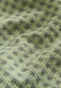 Nahaufnahme eines zerknitterten grünen Stoffes mit einem strukturierten Gittermuster aus kleinen erhabenen Kreuzen in dunkleren und helleren Farbtönen.