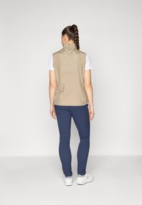 Beige vest with high collar, lightweight material, and a back vent, paired with navy pants and white footwear, viewed from the back.