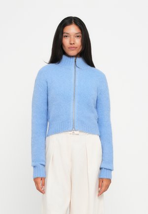 Light blue cropped zip-up sweater made of soft, fluffy material. Features a high collar and ribbed cuffs, creating a textured look.