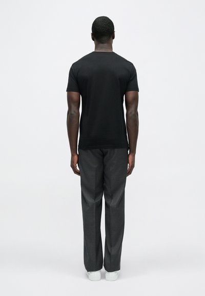 Μαύρο κοντομάνικο t-shirt με στρογγυλή λαιμόκοψη, σε συνδυασμό με γκρι καρό παντελόνι και λευκά αθλητικά παπούτσια, από πίσω όψη.