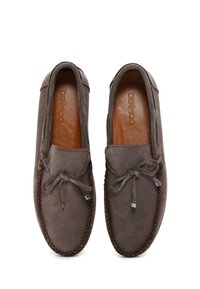 Mocasines de ante marrón con forro de cuero, detalle decorativo de lazo y costura en contraste a lo largo de la suela. Diseño plano, estilo fácil de poner.