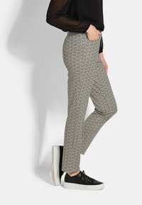 Texturierte, gemusterte Hosen in Schwarz und Weiß, mit einer mittelhohen Taille. Kombiniert mit schwarzen Sneakers mit weißen Sohlen.