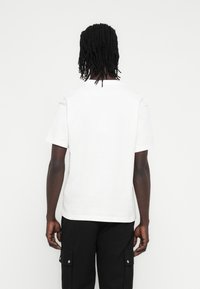 Λευκό βαμβακερό μπλουζάκι με κοντά μανίκια και στρογγυλή λαιμόκοψη, παρουσιάζεται από πίσω. Διαθέτει άνετη εφαρμογή και ομαλή υφή.