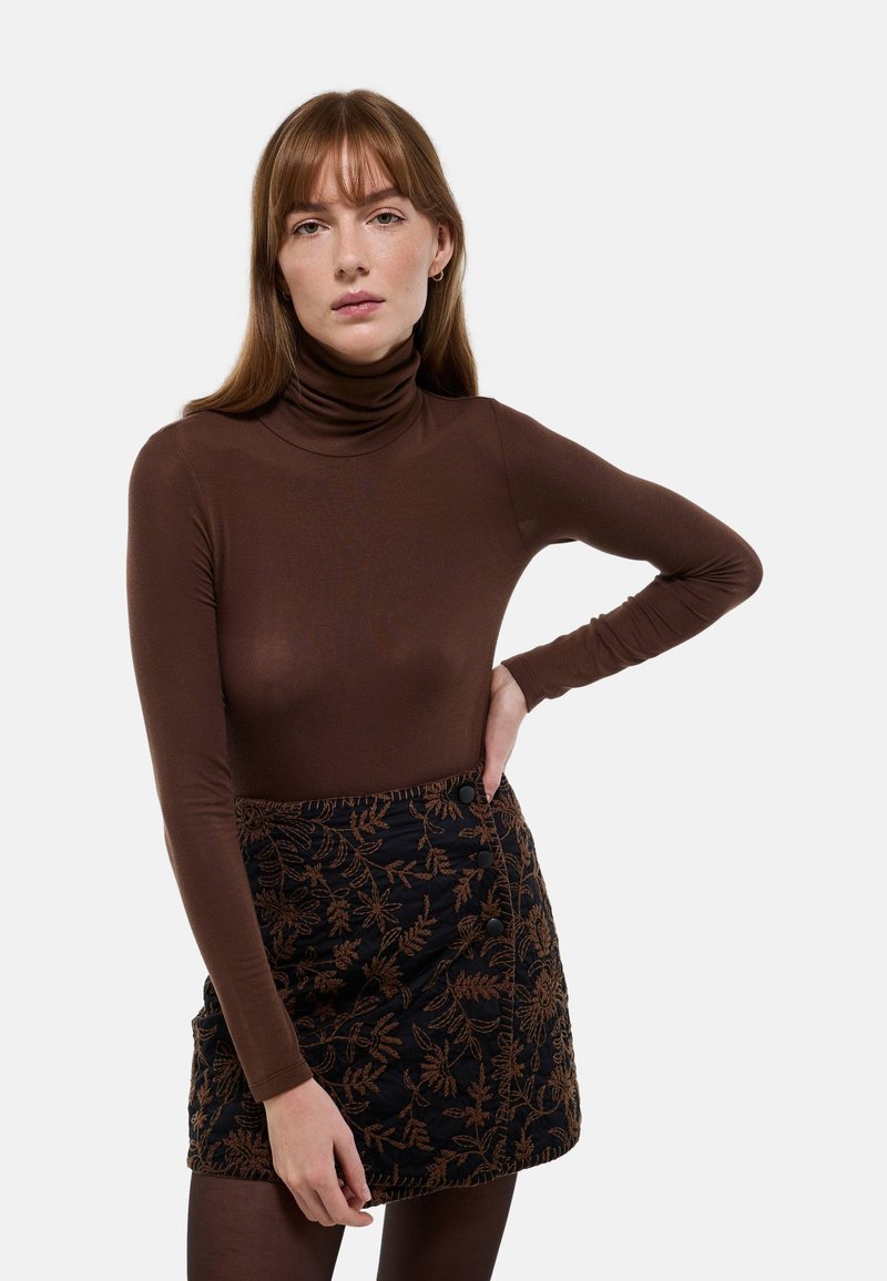 Top marron à col roulé avec des manches longues, associé à une jupe noire longueur genoux ornée de broderies florales marron et de boutons latéraux.