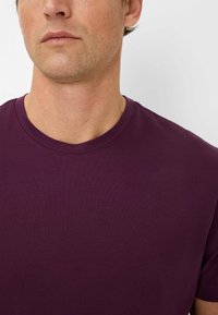 T-shirt in cotone viola a maniche corte con scollo rotondo, texture liscia e dettagli di cucitura minimi, con un focus sulla semplicità.