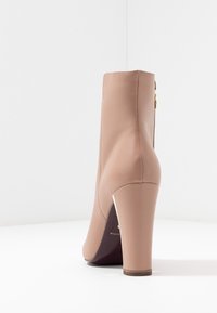 Nagie skórzane botki za kostkę o smukłym designie, wysokim obcasie w szpic oraz subtelnym złotym wykończeniu po boku. Gładka tekstura.