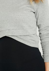 Top cinza de mangas longas com bainha curva, estilo sobreposto sobre leggings pretas de cintura alta. Tecido macio e suave com um ajuste casual.