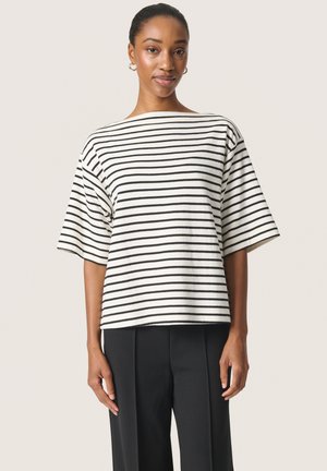 Gestreepte korte mouwen top in crème met zwarte horizontale strepen, met een brede boot halslijn en een relaxte pasvorm, gecombineerd met zwarte broeken.