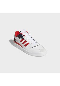 Baskets basses Adidas blanches avec des bandes rouges, un col de talon rouge, des accents noirs et des lacets blancs sur fond gris clair.