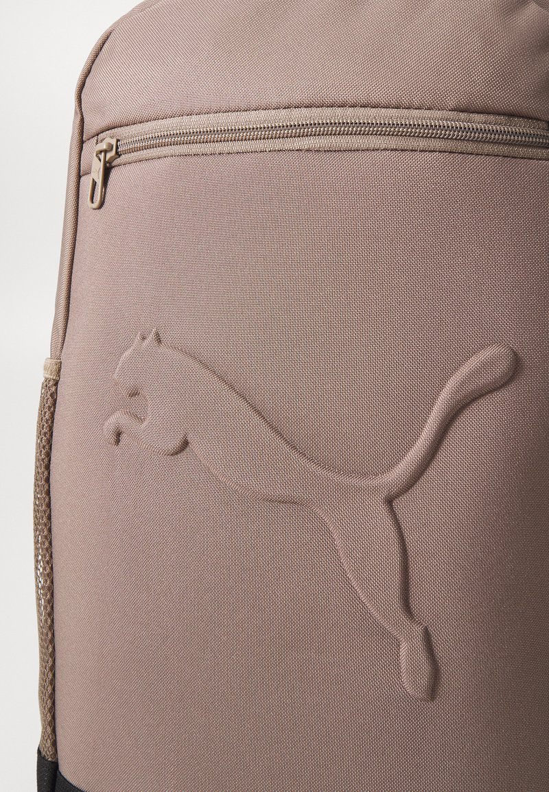 Zaino marrone realizzato in tessuto testurizzato, con un prominente logo Puma in rilievo, una tasca con zip e una tasca laterale in rete.
