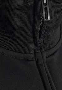 Gros plan sur un tissu noir texturé avec une fermeture éclair noire partiellement zippée et des coutures visibles le long des bords.