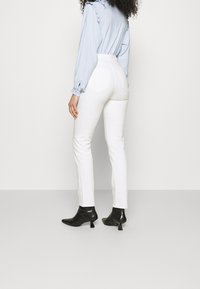Jeans bianchi a vita alta con una vestibilità slim, dotati di tasche posteriori e orlo alla caviglia, abbinati a stivaletti neri con punta. Blusa azzurro chiaro.