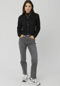Cardigan noir boutonné avec un tricot texturé et des accents argentés, associé à un jean gris taille haute et des baskets multicolores.