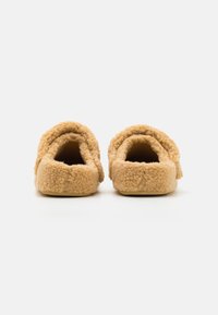 Chinelos cor de areia com uma textura suave e peluda e design de costas abertas. A sola é plana, permitindo um fácil calçar.