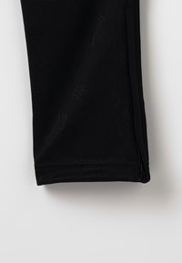 Schwarze Sporthose mit glatter Textur und einem dezenten Muster, Reißverschluss am Saum und sauber genähten Kanten.