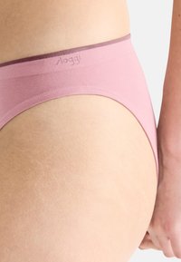 Różowa bielizna o gładkiej fakturze i fioletowym pasku z logo marki "sloggi". Design jest prosty i minimalistyczny.