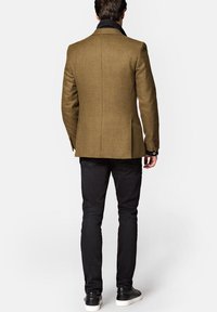 Brązowa marynarka w jodełkę o dopasowanym kroju, z czarnymi akcentami kołnierza i pojedynczym rozcięciem, zestawiona z czarnymi spodniami slim-fit i trampkami.