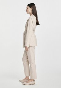 Beżowy garnitur dopasowany z paskiem w talii, spodniami o prostym kroju i prostymi balerinkami. Gładka tekstura i minimalistyczny design.