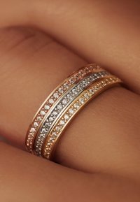 Trois anneaux empilés présentent des bandes en or rose, en argent et en or jaune, chacune ornée de petits gemmes clairs le long du bord supérieur.